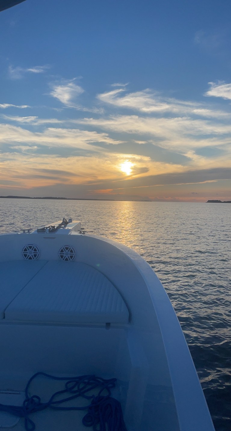 Boat on calm water at sunset with cloudy sky.
