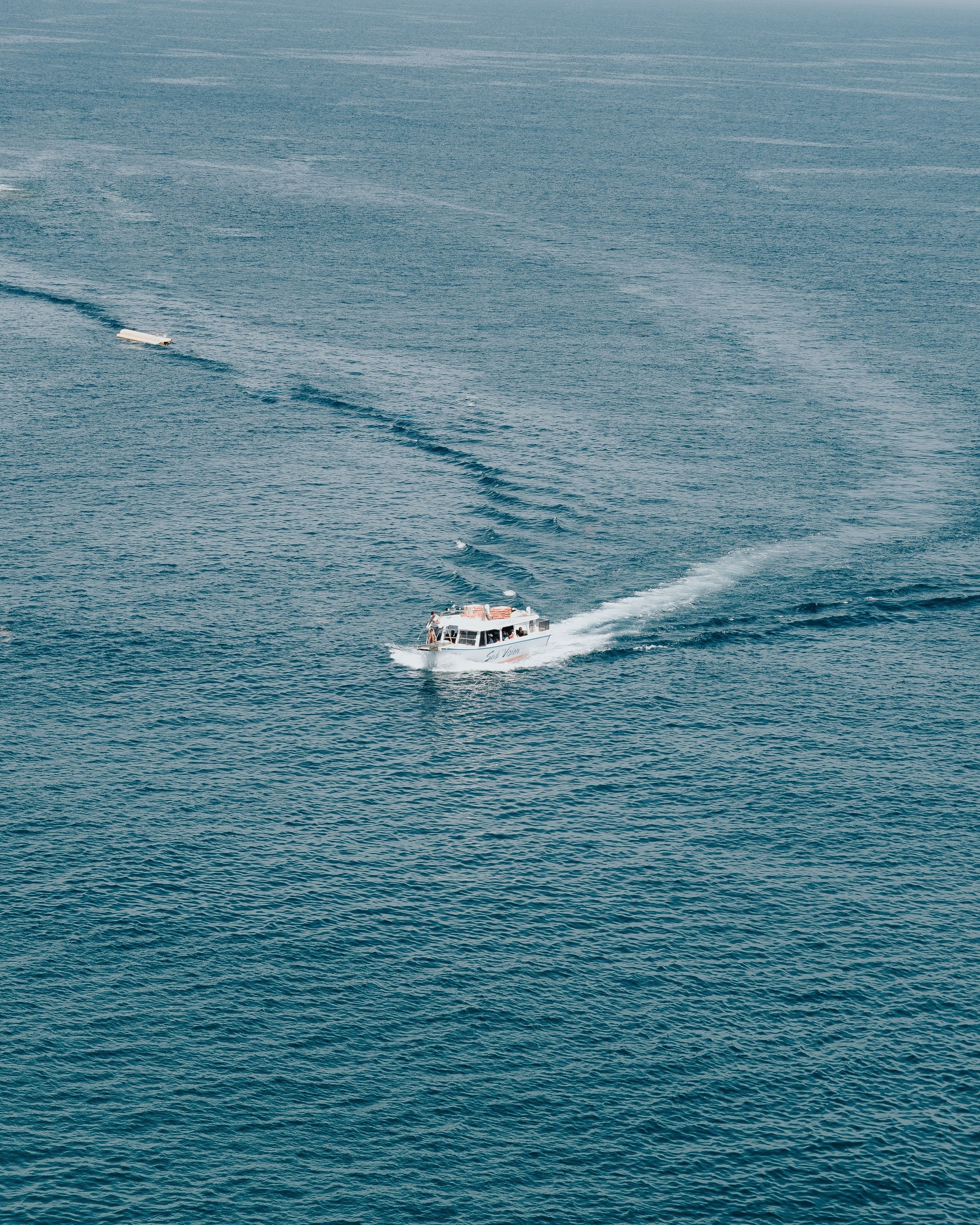 Boat sailing on vast open sea leaving a trail of wake in its path.