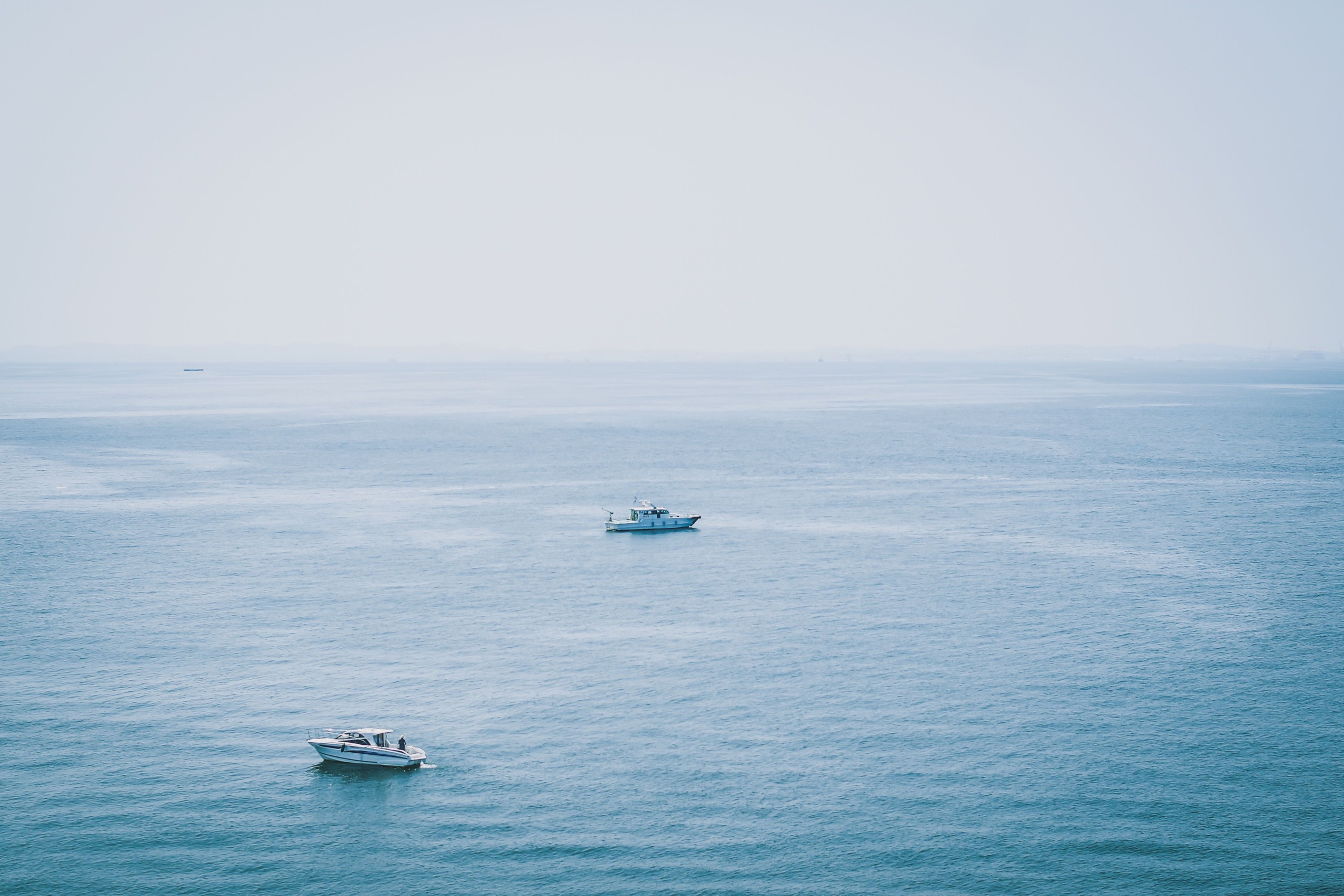 Two boats floating on a calm, expansive blue sea under a clear sky.